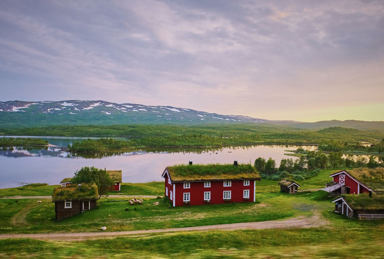 Typisch Zweeds rood huis met bijgebouwen en mos op het dak, uitzicht op een meer en bergen